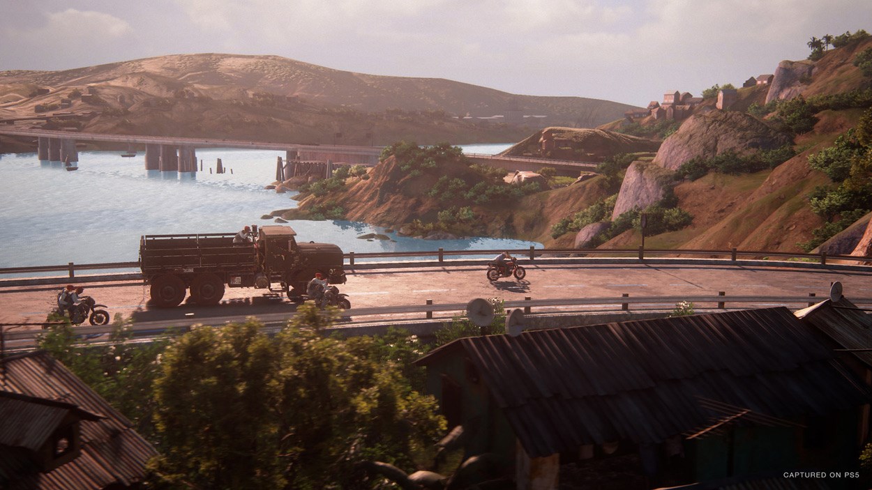 Two motorbikes and a truck travelling along a road next to a lake.