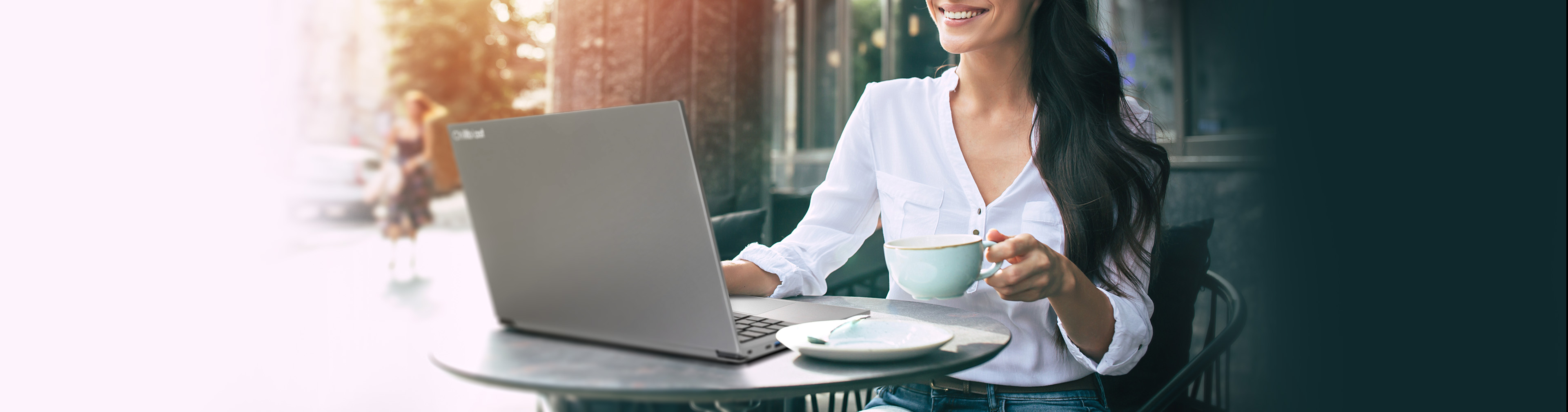 A woman using a Chillblast Phantom laptop at a coffee shop, coffee in hand.