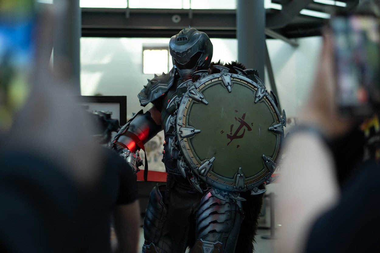 Olivier Richters in full DOOM Slayer armor holding the Shield Saw prop, surrounded by fans taking photos at the Royal Armouries Museum during the DOOM: The Dark Ages exhibition.