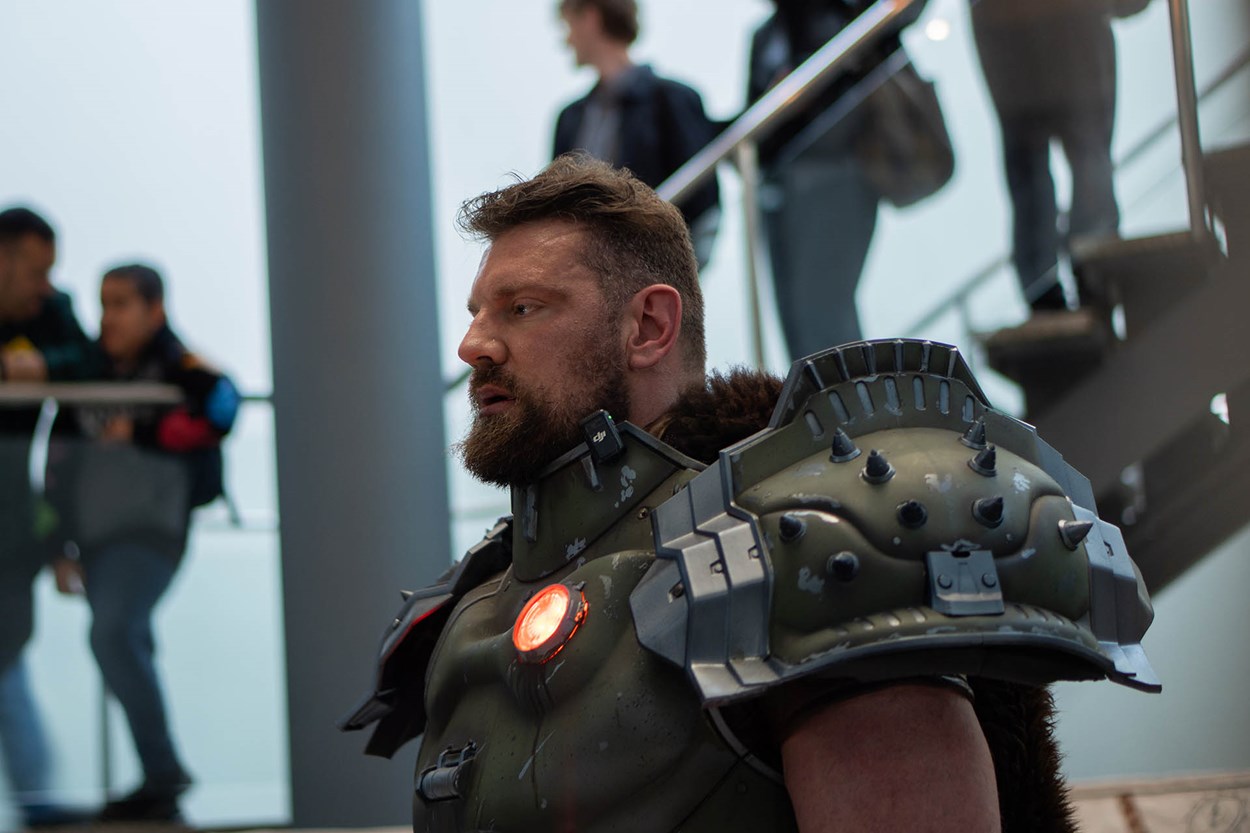 Actor Olivier Richters dressed as the DOOM Slayer, wearing detailed battle-worn armour with a glowing chest piece, standing inside the Royal Armouries Museum with onlookers in the background.