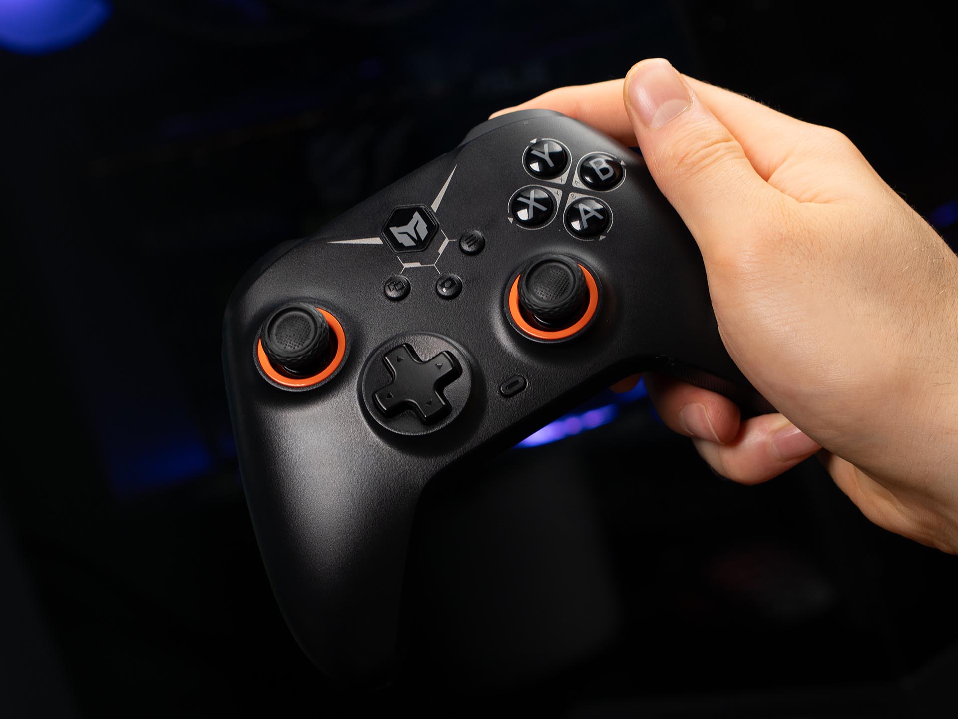 Hand holding a black BIGBIG WON Gale Hall wireless controller, highlighting its ergonomic grip and Hall-effect thumbsticks with orange accents.