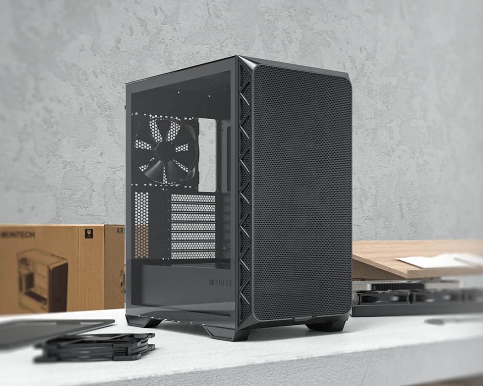 Montech Air 903 Base PC case with a mesh front panel and tempered glass side panel, displayed on a workbench with PC components and packaging in the background.