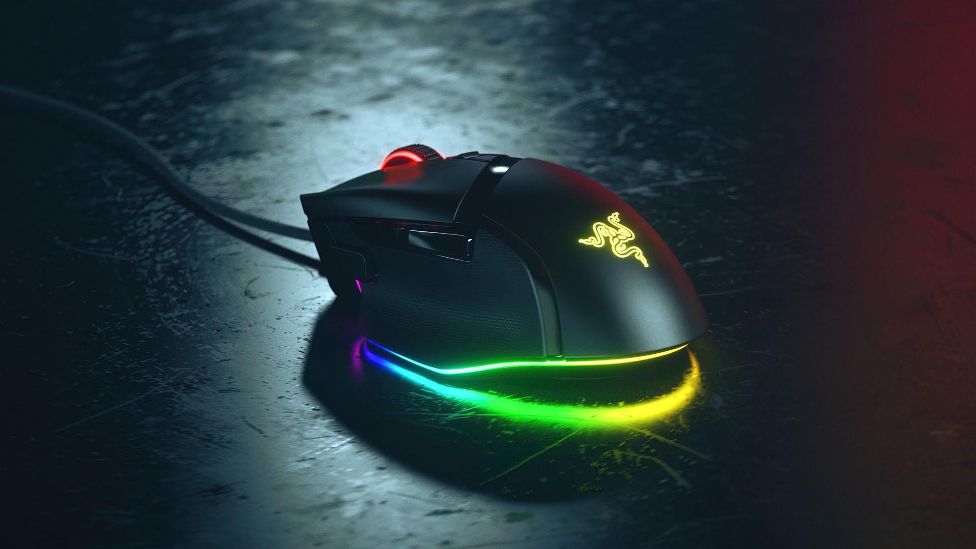 A Razer Basilisk V3 gaming mouse with bright RGB lighting glowing across the base, shown on a dark textured desk surface.