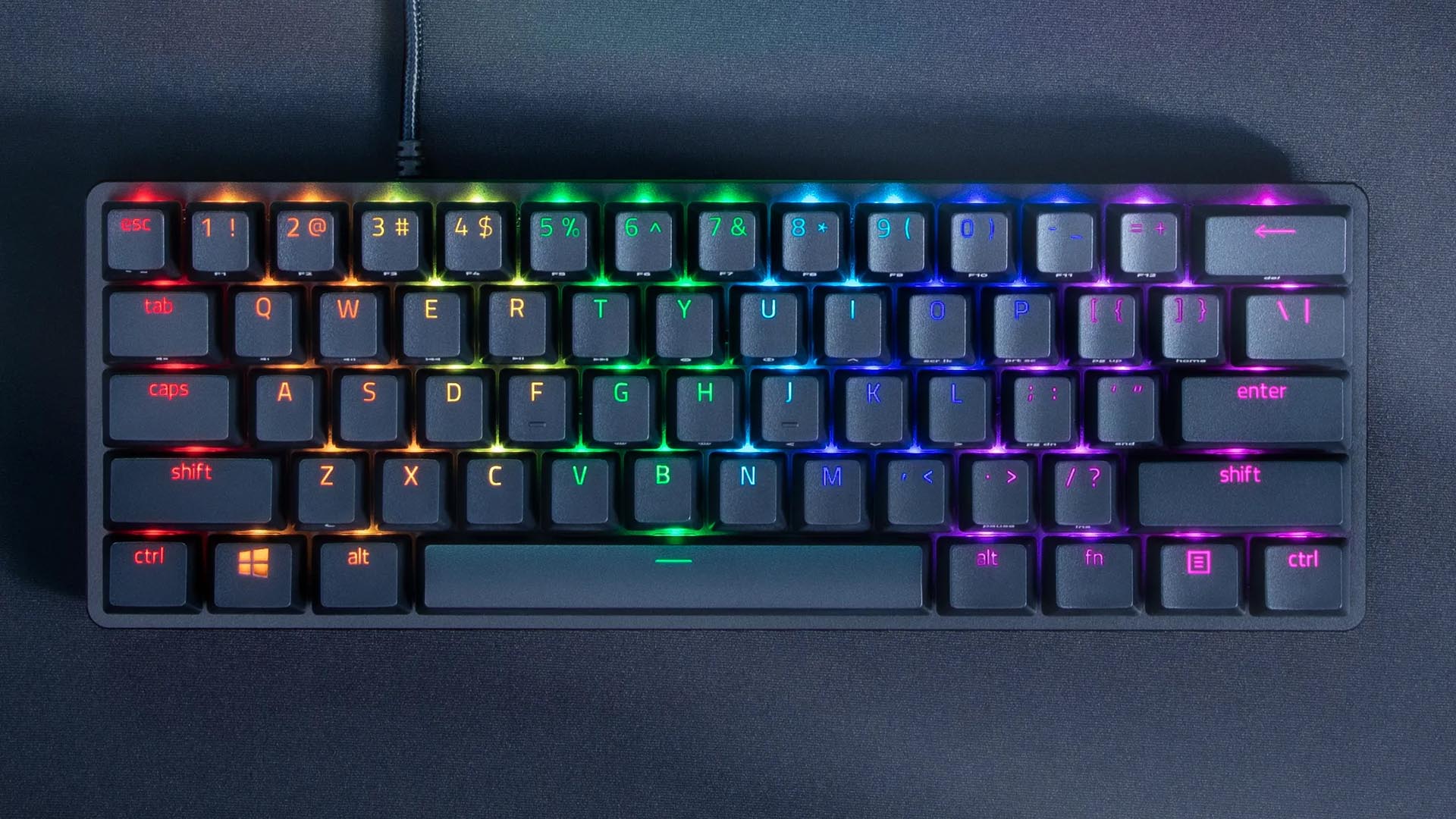 A Razer Huntsman Mini compact gaming keyboard with vibrant RGB lighting illuminating the keys on a dark desk surface.