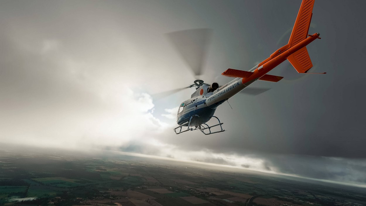 A helicopter flies through a cloudy sky above sprawling green farmland, with its orange tail rotor and sleek design contrasting against the overcast atmosphere.