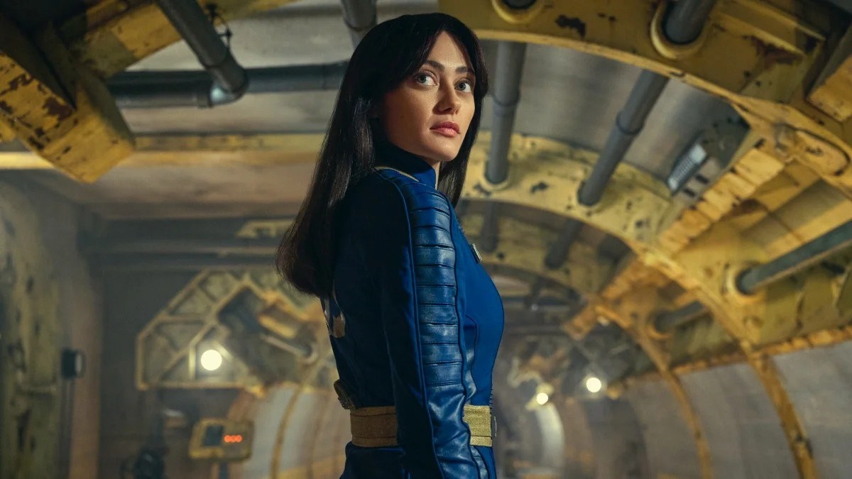 A woman in a blue Vault-Tec jumpsuit standing in a dimly lit, industrial underground setting from Fallout, winner of Best Adaptation at the 2024 Game Awards