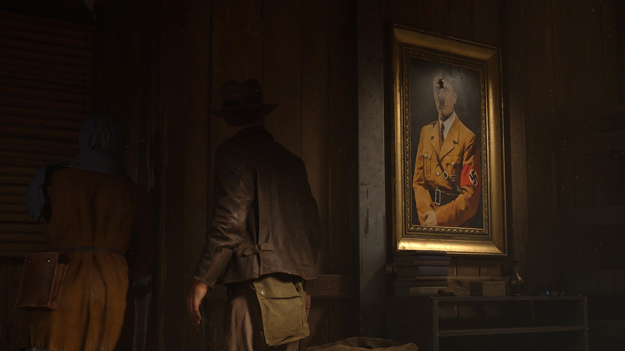 An adventurer wearing a leather jacket and fedora stands in a dimly lit room beside a portrait of Adolf Hitler, suggesting a tense and historical narrative setting.