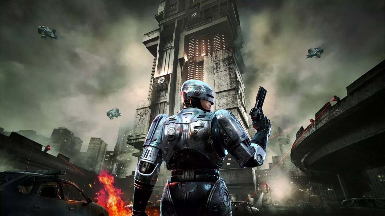 RoboCop stands armed in a dystopian city as helicopters and laser-equipped enemies surround a towering fortress in the background, with fire and destruction in the streets below.