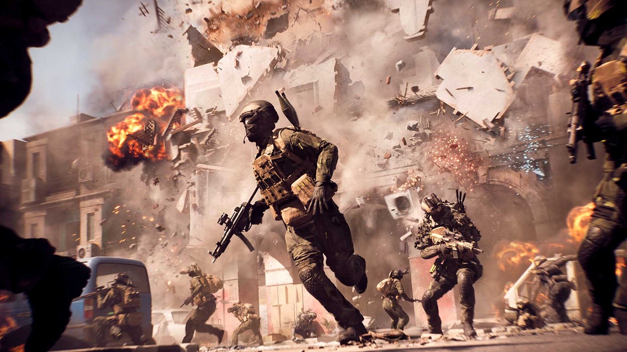 Soldiers sprint through a war-torn city street as a nearby building explodes, sending debris and fire into the air during intense urban combat.